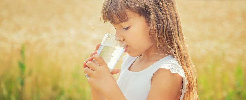 A child drinks water on the background of the field. Selective focus.