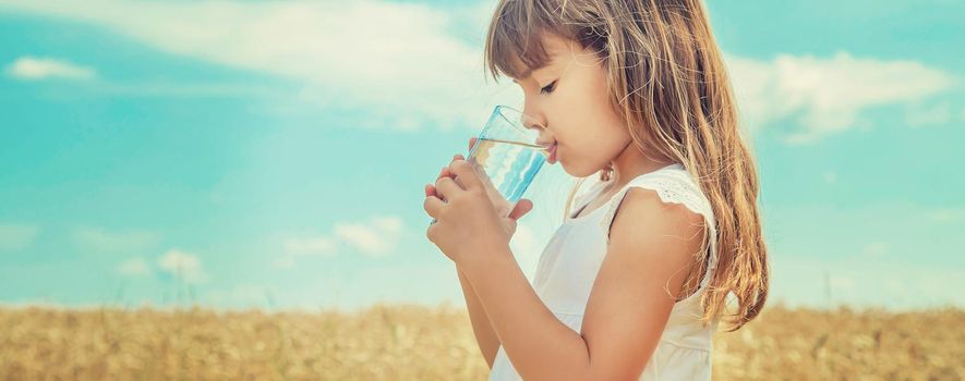 A child drinks water on the background of the field. Selective focus.