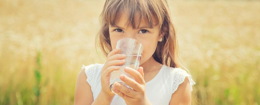 A child drinks water on the background of the field. Selective focus.