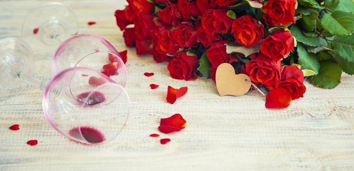 A bouquet of red roses and red wine in glasses. Valentine's Day. Selective focus. Holiday.