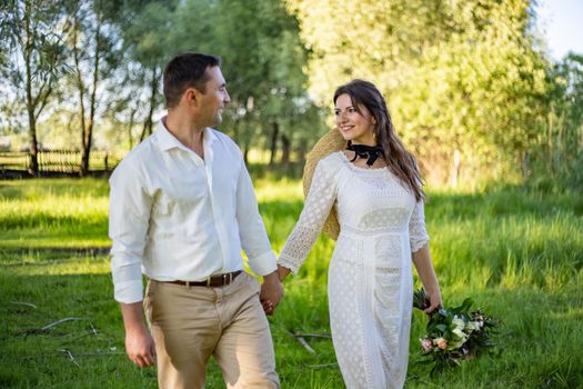 Just married loving hipster couple in wedding dress and suit on a green field in the woods. happy bride and groom walking running and dancing on a summer meadow. Romantic married to a young family.