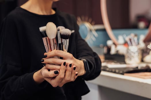 Unrecognisable Female Make Up Artist Holding in Hands Brushes, Workplace on Background in Beauty Salon
