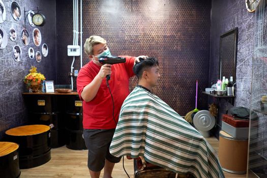 Profile of a obese barber standing while drying the hair of an asian gay client in a barber shop