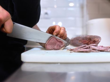 Close up view of cook's hands slicing fish with a big knife in a restaurant kitchen