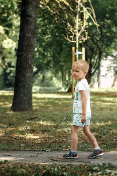 A sad lonely little boy walks in a city park. The child got lost he was looking for his parents.