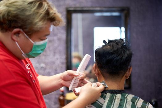 Focus on the hands of a barber shaving the nape of a client using a clipper and comb