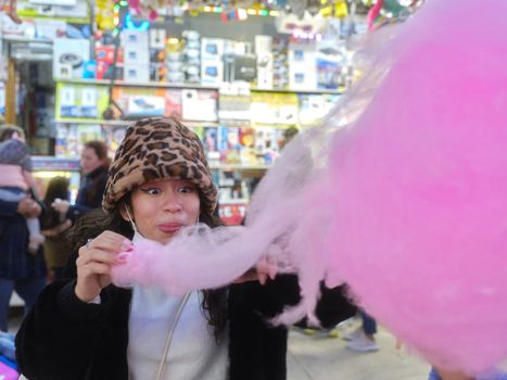 Latin woman with expression of happiness eating a cotton candy in an amusement park at night