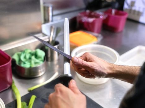 Close up view of the hands of a cook sharpening kitchen knives with a hand-held sharpener