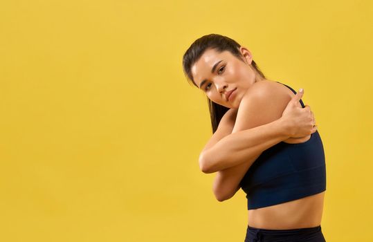Young woman in black top tight hugging herself, thoughtfully looking at camera. Portrait view of serious girl wrapping arms around body in hug, isolated on orange background. Concept of mindfulness.