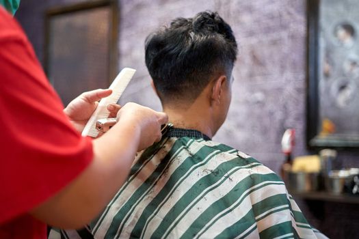 Back of a client sitting on a chair while a barber shaving her nape in a barber shop