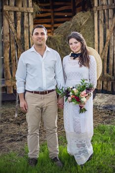 Loving groom in a black cardigan and a cute bride in an expensive dress are hugging, sitting in the forest on the nature. Wedding portrait of smiling newlyweds. Photography, concept