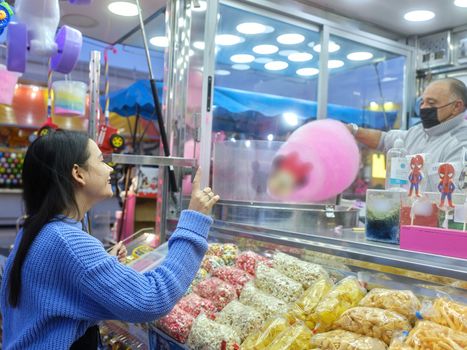Woman ordering one cotton candy in a fair stall at night
