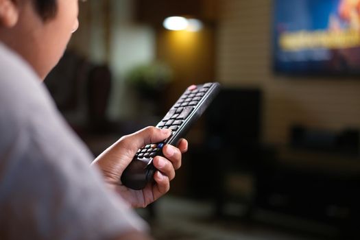 teenage boy hand holding tv remote sited on sofa .