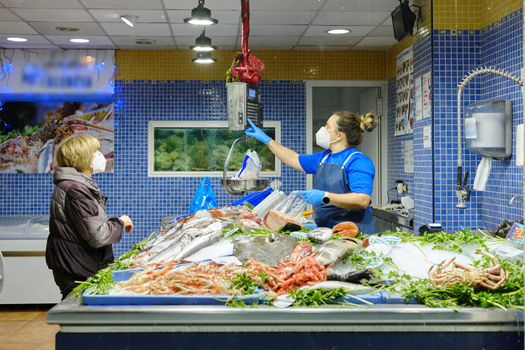 Woman with mask buying fish to a fish vendor with mask in a fish store in a market