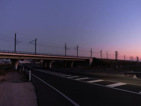 Panoramic photo of a railway bridge crossing a highway at sunset