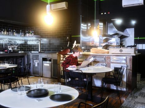 Female manager of a restaurant working inside the establishment seated at one of the tables