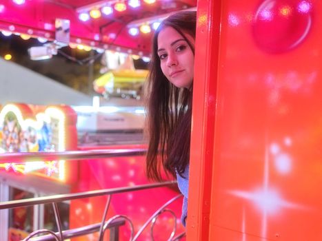 Woman sticking her head out of a column of a fair attraction while looking to the camera at night