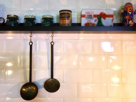 Kitchen utensils hanging on the kitchen of a restaurant next to a shelf with spices and objects