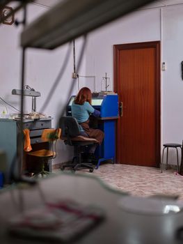 Vertical image of an unrecognizable adult woman working sitting in a polishing machine with a safety box in her jewelry workshop.