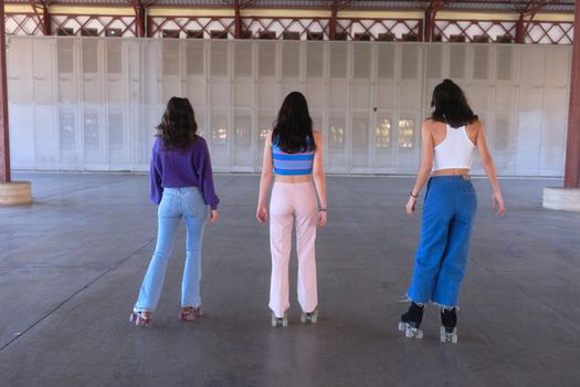 Back of three fit young caucasian women wearing vintage clothes skating on an urban area in summer