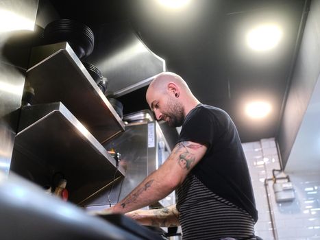 Counter view of a cook wit tattoos working on a kitchen of a restaurant