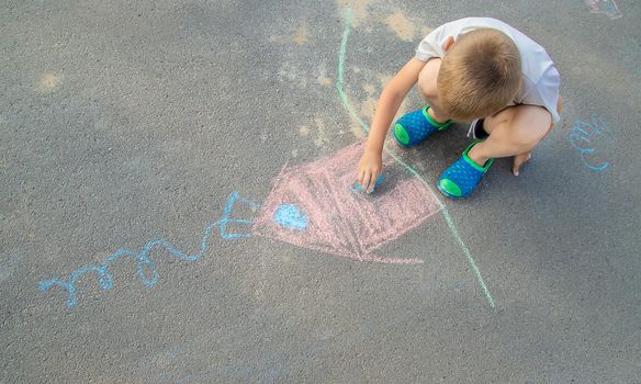 child draws a house in chalk on the pavement. Selective focus. nature.