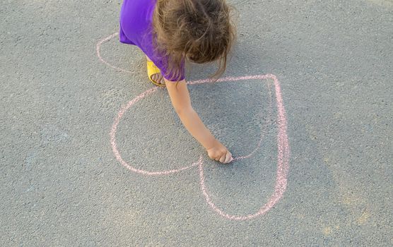 the child paints chalk on the asphalt heart. Selective focus. Draw.