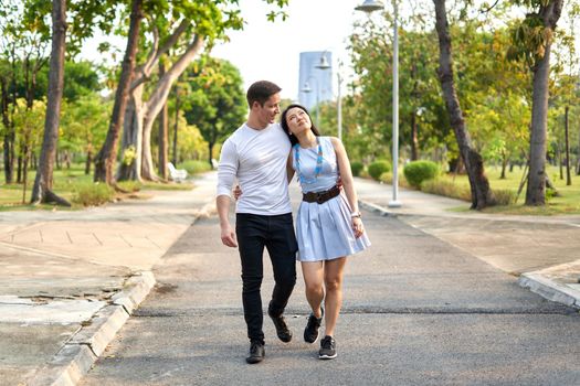 newly married multiethnic couple strolling through a city park during sunset in summer