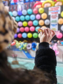 Vertical photo with focus on a woman's hand throwing a dart at a night-time fair