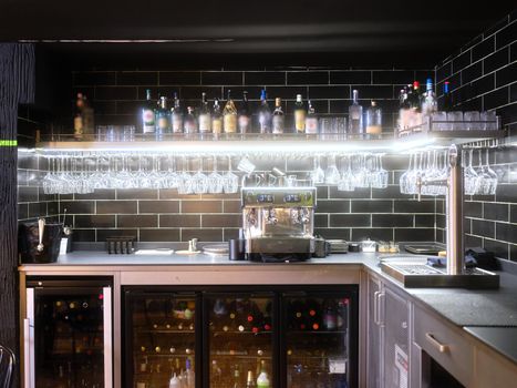 Illuminated restaurant bar with glasses hanging from a rack and bottles of wine in the fridge