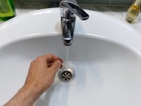 Top view of a hand of a a man on a sink with water running out of the faucet