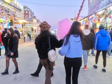 Two latina women walking among an outdoors fair eating a pink cotton candy at night