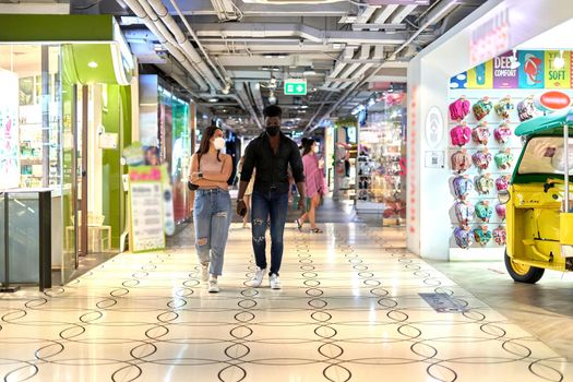 Multiethnic friends wearing mask and walking relaxed through a shopping mall passage between shops