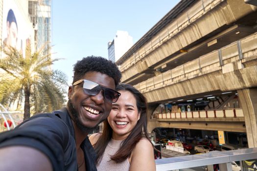 Two mutiethnic smiling friends embracing while taking a selfie outside a shopping mall