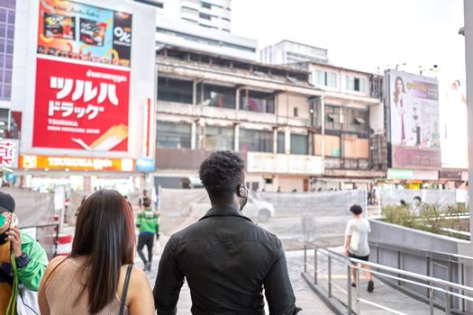 Back of two multiracial friends walking outside a mall with advertising posters in Bangkok, Thailand