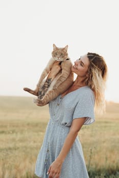 Caucasian Young Woman Dressed in Blue Dress Holding Her Cat Outdoors at Sunset