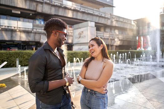 Two multiracial friends chatting in front of water fountains in a shopping mall in Bangkok