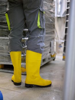 Vertical photo of the legs of a worker wearing protective boots in a craft beer packaging factory