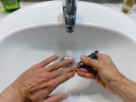 Top view of the hands of a man cutting his nails on a bathroom sink using a nail clipper