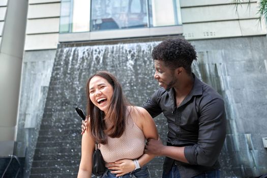 Portrait of an asian woman laughing next to an african friend outside a modern shopping mall