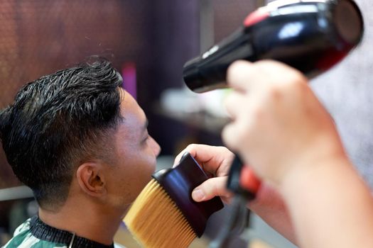 Focus on the head of a client while a barber drying her hair with a hand-held hairdryer