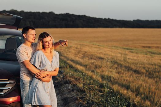 Cheerful Young Couple Hugging Near Car, Caucasian Woman and Man Enjoying Road Trip at Sunset, Copy Space