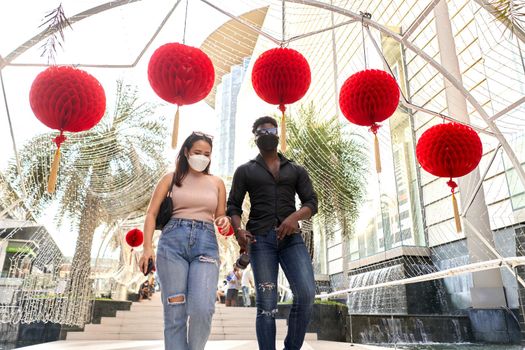 Two multiethnic friends wearing mask walking in a mall decorated with red lanterns in Bangkok