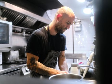 Selective focus on a cook with tattoos working inside a kitchen while wearing an apron