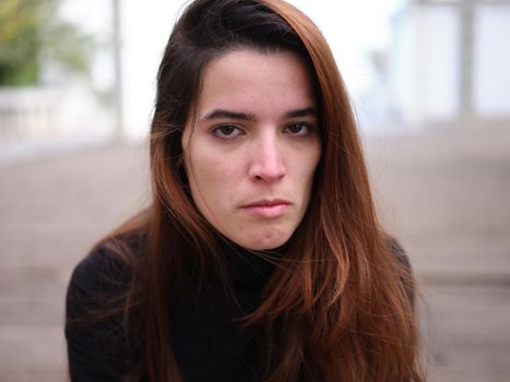 Portrait of an angry young woman looking hatefully at the camera with an blurred background. Concept of emotions.