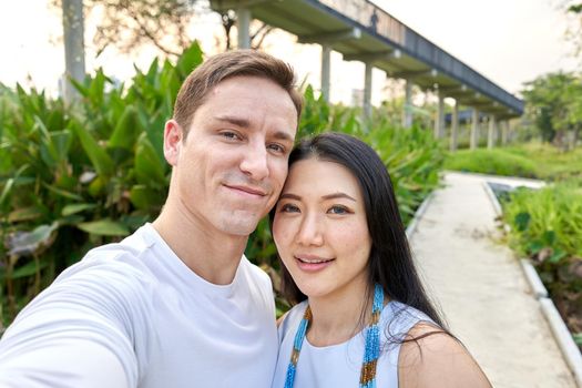 Newlyweb multicultural couple taking a selfie in a uran park with a bridge during sunset