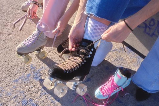 Cropped photo of the hands of two caucasian women lacing up their skates outdoors in a sunny day