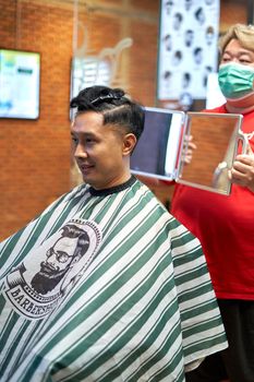 Fat barber with mask showing the back of the head to a gay customer using a mirror in a barber shop