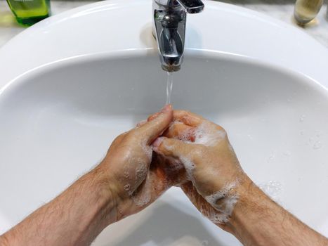 Top view of a person washing hands with soap on a bathroom sink