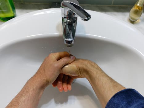 Top view of the hands of a man washing his hands in the sink of a bathroom